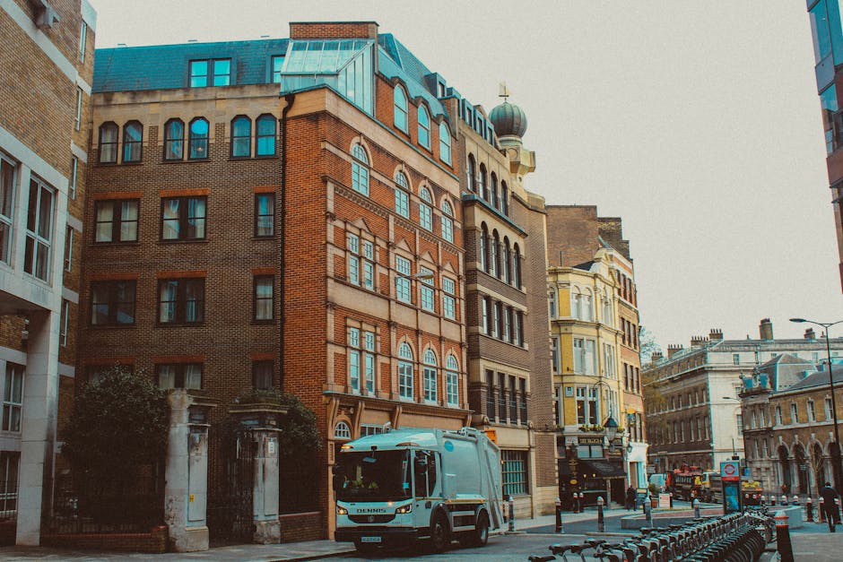 A street scene in South Kensington featuring a white removal truck parked on the pavement near a row of historic multi-storey buildings with brick and stone facades, large windows, and decorative arch