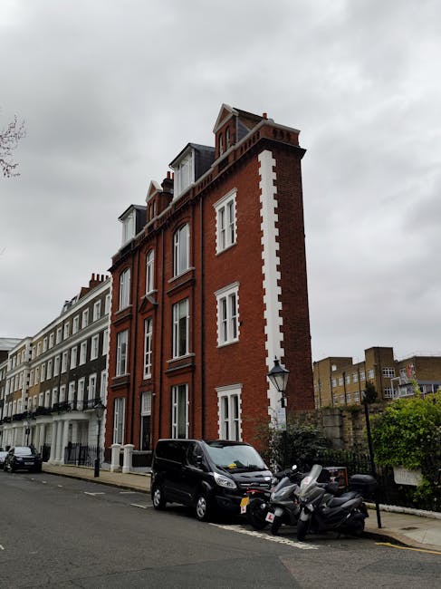 A street scene in South Kensington featuring a white removal truck parked on the pavement near a row of historic multi-storey buildings with brick and stone facades, large windows, and decorative arch